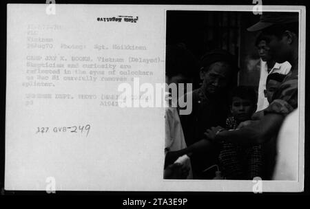 Soldier providing medical care by removing a splinter during a MEDCAP in Vietnam. The photo taken on August 26, 1970, at Camp Jay X. Books shows the skepticism and curiosity onlookers had while witnessing the procedure. Image source: Defense Department, taken by Sgt. Heikkinen. Stock Photo