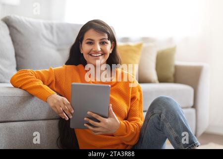 Happy indian woman sitting on floor at home, using tablet Stock Photo