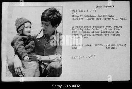 Title: Vietnamese Refugees Smile Upon Arrival at Camp Pendleton, California Caption: A Vietnamese refugee boy, held by his father, smiles after arriving at Camp Tulega on April 29, 1975. Claudia Cardinale, Nguyen Cao Ky, Rosemary Clooney, and Betty Ford were among the visitors during the event. The photograph was taken by Major G.L. Gill and is credited to the Defense Department/Marine Corps. Stock Photo