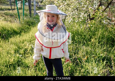 A little girl in a beekeeper costume helps in an apiary caring for bees Stock Photo