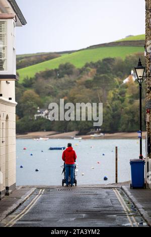 Man in red top standing atop the harbour wall with his back to camera, and pushchair in front of him, looking out toward East Portlemouth beach. Stock Photo