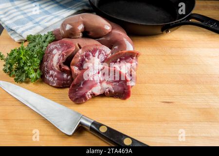 Raw fresh lambs kidneys preparation on a wooden cutting board in a home kitchen getting ready to sauté or fry in butter Stock Photo