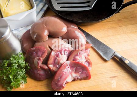 Raw fresh lambs kidneys preparation on a wooden cutting board in a home kitchen getting ready to sauté or fry in butter Stock Photo