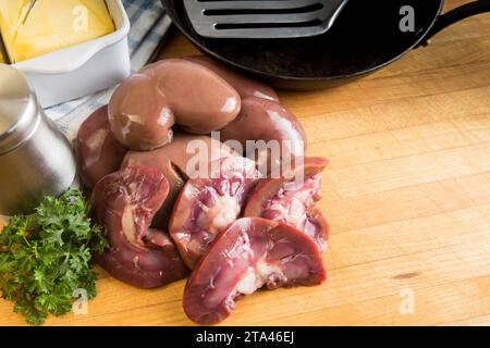 Raw fresh lambs kidneys preparation on a wooden cutting board in a home kitchen getting ready to sauté or fry in butter Stock Photo