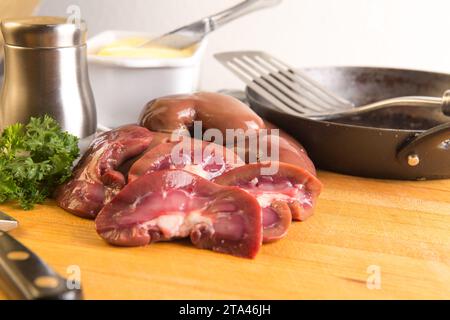 Raw fresh lambs kidneys preparation on a wooden cutting board in a home kitchen getting ready to sauté or fry in butter Stock Photo