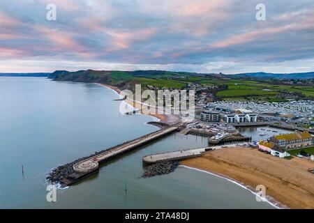 West Bay, Dorset, UK.  28th November 2023.  UK Weather.  The clouds are tinged pink during sunset above the seaside resort of West Bay in Dorset at sunset at the end of a cold and cloudy afternoon.  Picture Credit: Graham Hunt/Alamy Live News Stock Photo