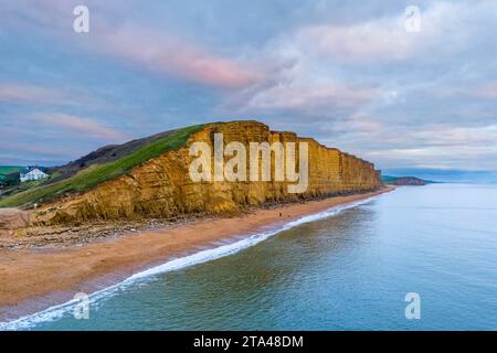 West Bay, Dorset, UK.  28th November 2023.  UK Weather.  The clouds are tinged with pink at sunset above the cliffs at West Bay in Dorset during sunset at the end of a cold and cloudy day.  Picture Credit: Graham Hunt/Alamy Live News Stock Photo