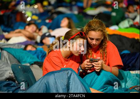 Two girls looking at a phone before sleep. The Vigil in Parque Tejo – Campo da Graça. World Youth Days 2023 in Lisbon, Portugal. Stock Photo