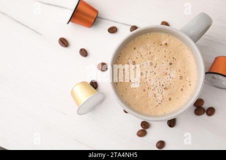 Cup of coffee, capsules and beans on white wooden table, flat lay. Space for text Stock Photo