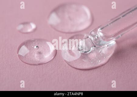 Dripping cosmetic serum from pipette onto pink background, macro view Stock Photo