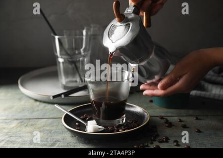 Woman pouring coffee from moka pot into glass at rustic wooden table, closeup Stock Photo