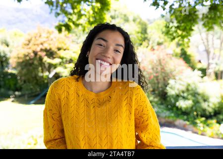 Portrait of happy biracial woman in yellow sweater in sunny nature Stock Photo