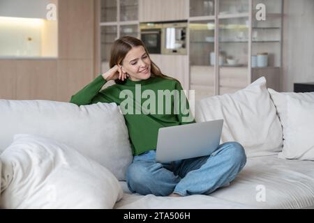 Happy woman watching movie, series or video on laptop sitting on couch at home. Stock Photo