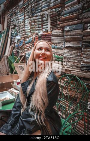 Smiling woman sitting in front of a wall of literature and fiction books in Venice. Stock Photo
