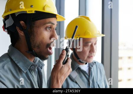 Contractor using walkie-talkie when controlling work of building at construction site Stock Photo