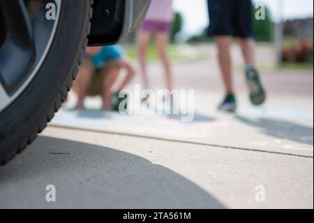 Children sitting on a driveway behind a vehicle in a blind spot out of view of the driver.  Stock Photo