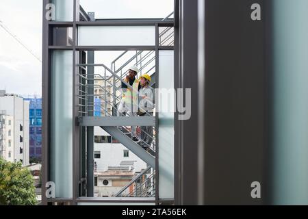 Engineer and foreman standing on stairs outside building and using walkie-talkie to communicate with team on construction site Stock Photo