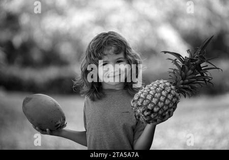 Child boy holding pineapple and coconut smiling with happy face. Summer fruits. Stock Photo