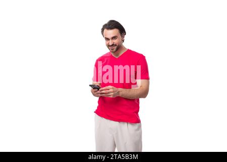 a young brutal black-haired man dressed in a red corporate T-shirt uses a mobile phone Stock Photo