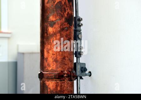 shiny new copper rain water leader, downspout or down pipe detail. lightning protection grounding rod. home renovation, construction. stucco elevation Stock Photo