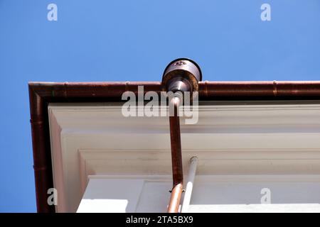 shiny new copper gutter rain water leader, downspout detail. home renovation and construction closeup. textured stucco exterior. roof edge. blue sky Stock Photo