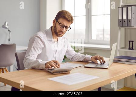 Focused businessman working on accounts using a calculator and laptop Stock Photo