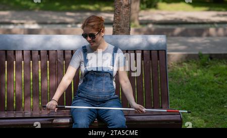 Blind red-haired pregnant woman sitting on a bench outdoors.  Stock Photo