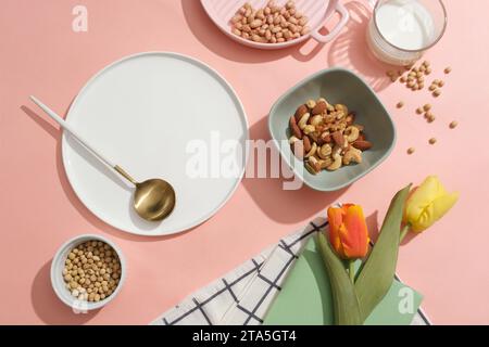 Various nuts and beans are arranged over pink background. Ceramic dish with blank space to show your product extracted from organic nuts and beans Stock Photo