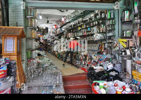 A merchant works in her shop, stocked from floor to ceiling and overflowing out to the sidewalk with dishes, glassware and more in Hanoi, Vietnam Stock Photo