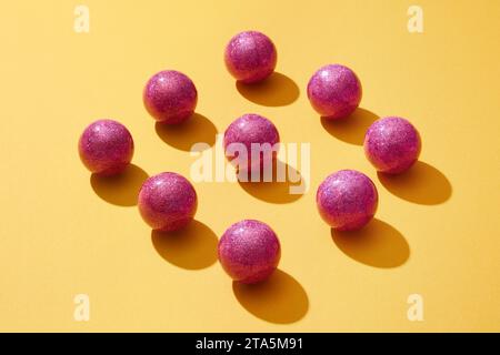 On the yellow background, sparkling purple baubles are arranged neatly into a rhombus shape. Symbolic ornament for Christmas. Baubles bring strength a Stock Photo