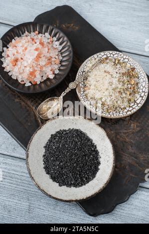 different types of salt. Three different types of salt in handmade craft plates on a clay board. White herbal sea salt, pink Himalayan and black Maldo Stock Photo