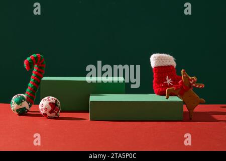 Advertising scene with Christmas concept. Green empty podiums decorated with cute woolen accessory on green and red background. Front view, space for Stock Photo