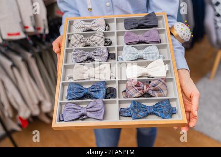 saleswoman holding a tray of various bow ties with a rack of suits in the background on a store Stock Photo