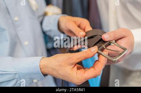 Close-up of hands holding a black leather belt with a silver buckle in a wedding store Stock Photo