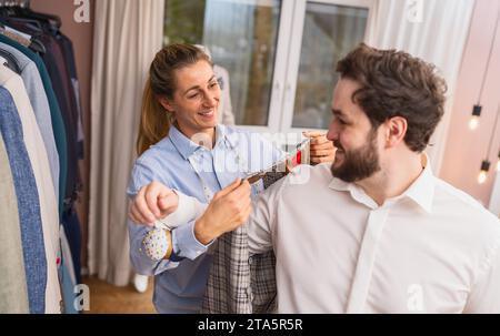 Tailor with measuring tape fitting a jacket on a male client at shop Stock Photo