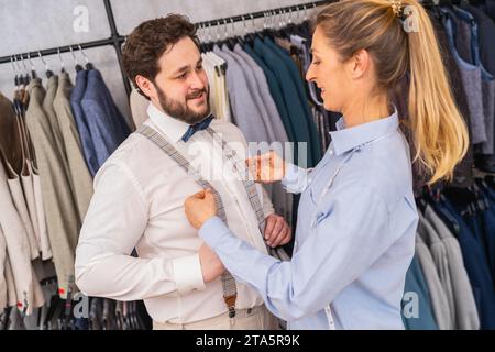 Tailor adjusting a man's suspenders, both looking at each other and smiling Stock Photo