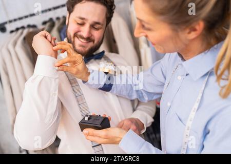 Tailor helping a man with cufflinks, both sharing a joyful moment Stock Photo