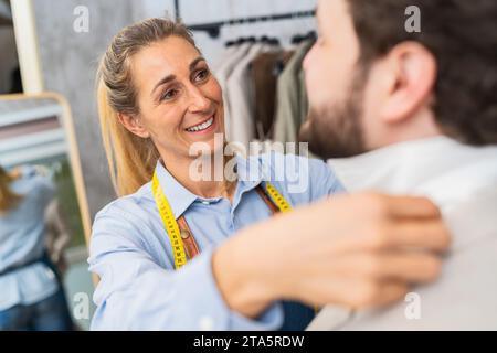 Tailor woman fitting a shirt on a male client, both smiling in a shop Stock Photo