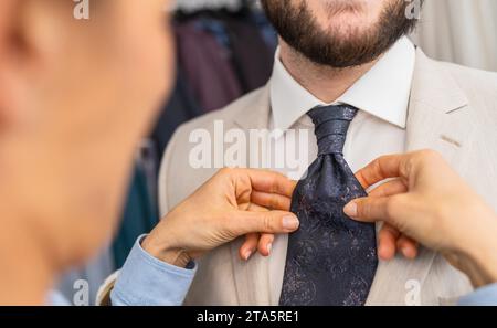Saleswoman adjusting a tie on a man in a beige suit Stock Photo
