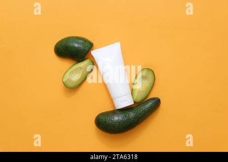 Against the yellow background, an empty plastic tube decorated with fresh slices of avocado slices. Mockup packaging, cosmetics design. Minimalist con Stock Photo