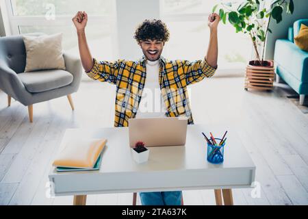 Photo of glad cheerful positive man sitting table completing finishing tasks project startup shouting yes hooray indoors Stock Photo