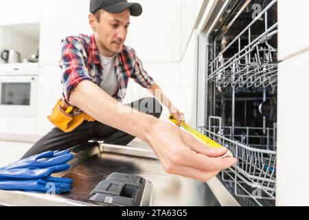 Worker using screwdriver to repair dishwasher at home stock photo Stock Photo