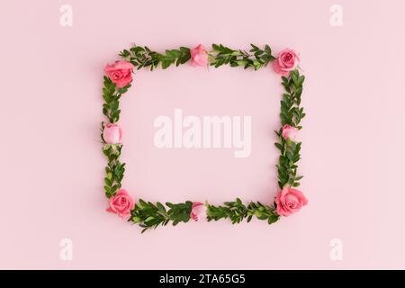 Floral wreath made of pink roses and green branches on a pink background. Stock Photo