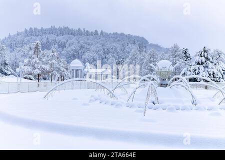 Snow-covered singing fountain with the Carolina Spring Colonnade (Kolonáda in Czech) in the background - center of spa town Marianske Lazne (Marienbad Stock Photo