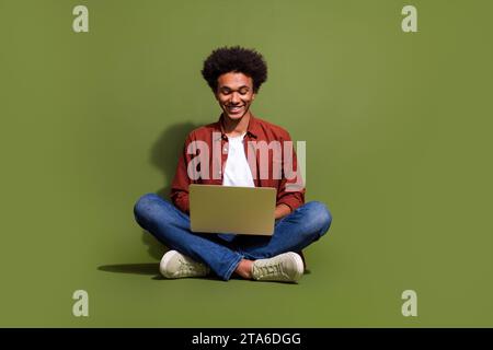 Full size photo of handsome young guy sit floor working netbook remotely wear trendy brown outfit isolated on khaki color background Stock Photo