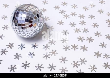 The disco ball lies on a white background strewn with silver snowflakes. New Year and Christmas background. Stock Photo