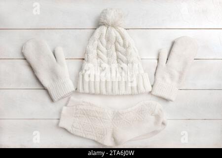 A white knitted hat with a pompom, woolen mittensa nd socks lie on a white wooden background. Details of winter clothing, flat lay, top view Stock Photo