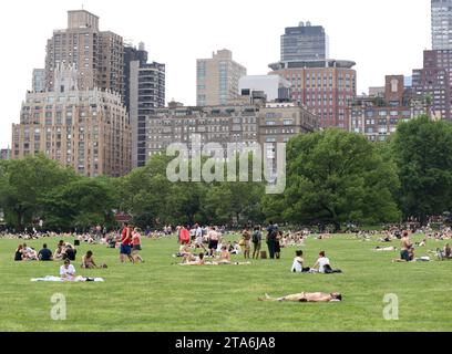 New York, USA - May 26, 2018: People relax on Sheep Meadow in Central Park and skyscrapers of the Manhattan at the background. Stock Photo