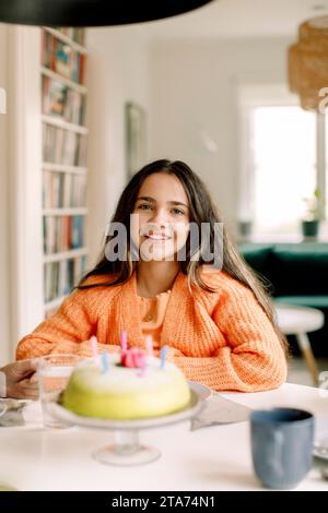 Girl sitting at table with birthday cake, smiling at camera Stock Photo ...
