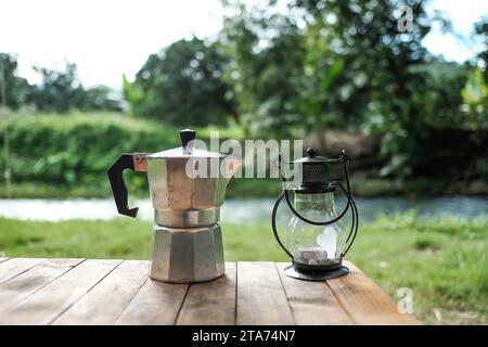 Vintage electric lantern and glass dripper carafe on a folding table for camping at river side blur background Stock Photo